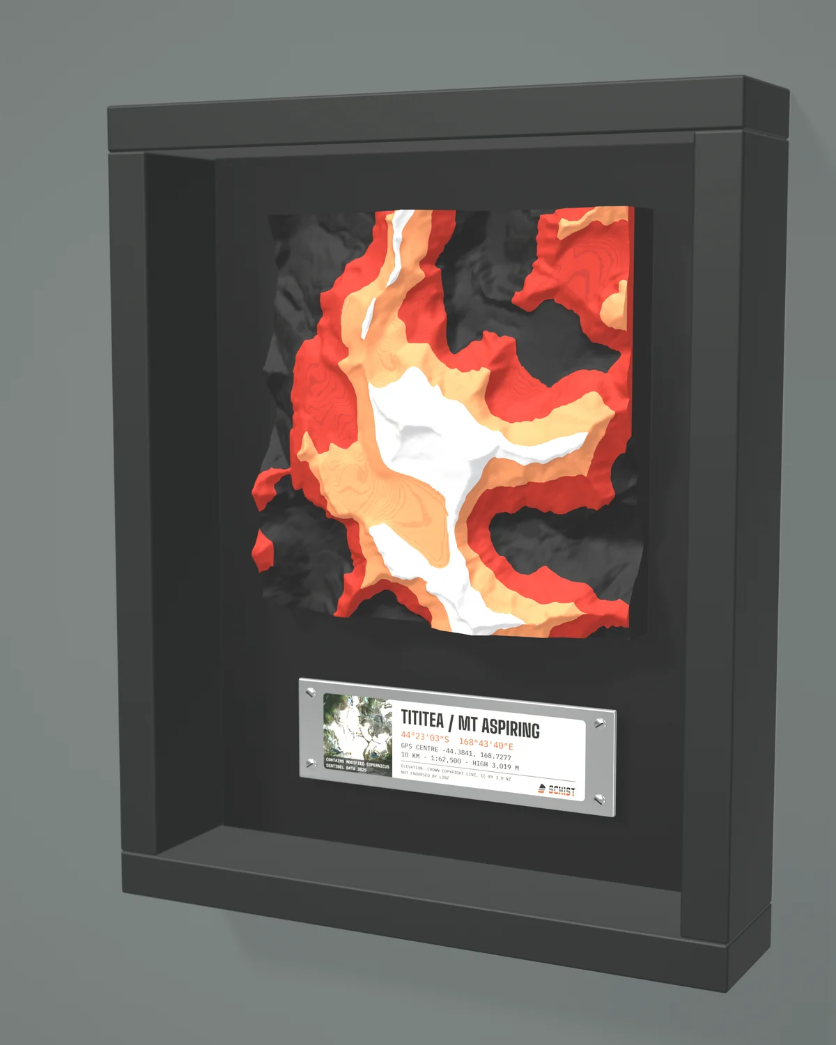 Render: the Tititea / Mt Aspiring tile in Ember colours inside a painted black shadow-box frame on a black backing, with a metal plate below giving the place name, GPS centre, scale, a small satellite image and the data credits.