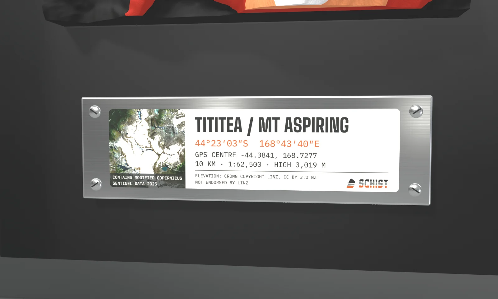 Render, close-up: the metal plate under the Tititea tile, with a satellite square credited 'Contains modified Copernicus Sentinel data 2025', the name Tititea / Mt Aspiring, its coordinates, scale and high point, an elevation credit to LINZ under CC BY 3.0 NZ, and the SCHIST logo.