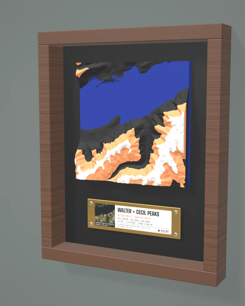 Render: the Walter + Cecil Peaks tile in Alpenglow colours, Lake Wakatipu in blue, in a walnut-look frame with a brass-look plate.